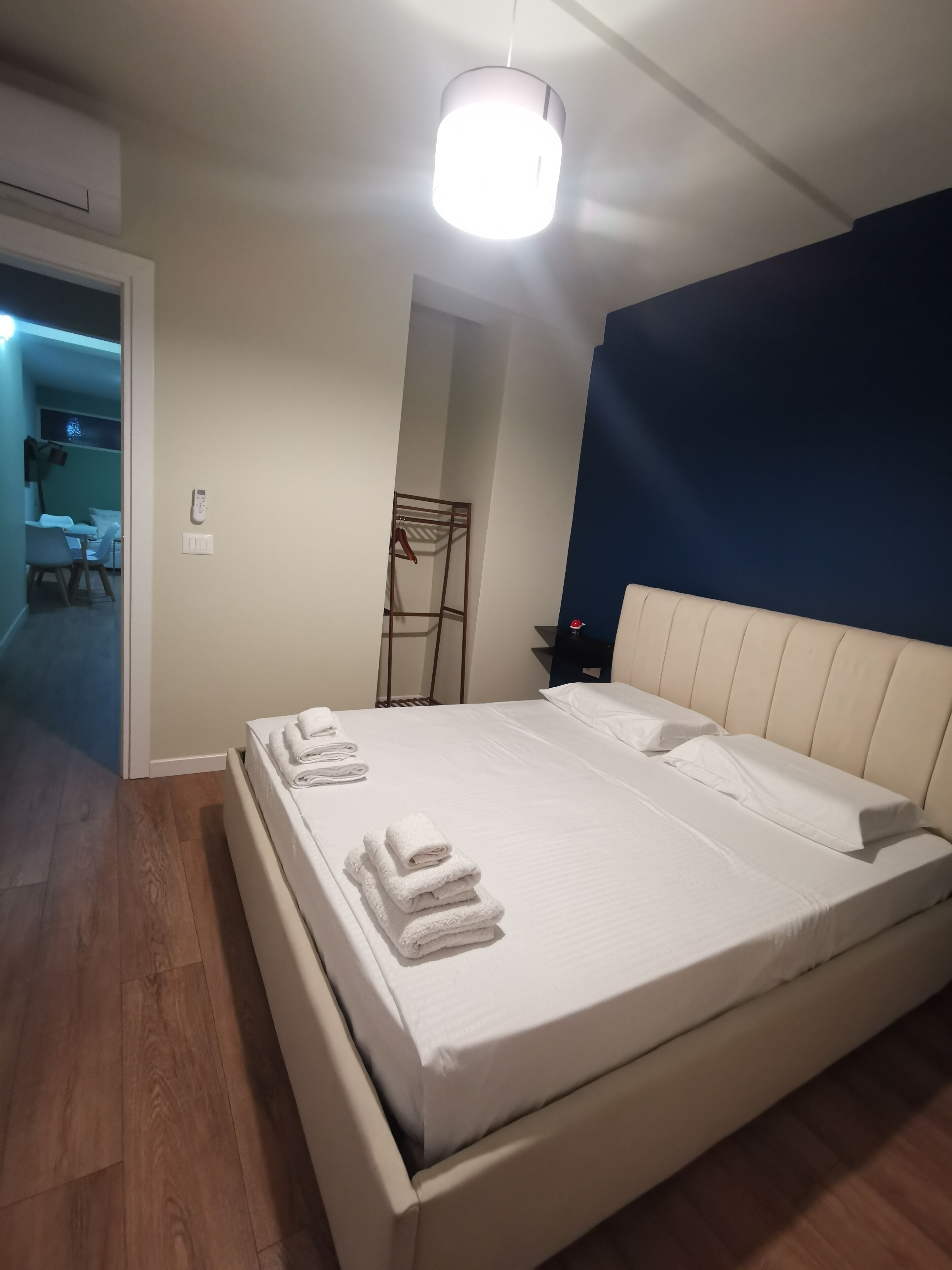 A neatly made bed with white linens and towels, a bedside table with a lamp, and a blue accent wall.