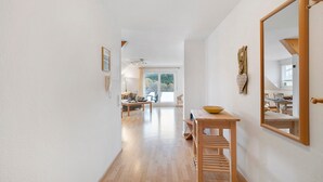 Un pasillo con una mesa de madera y un espejo a la derecha, que conduce a un área de comedor con luz natural.