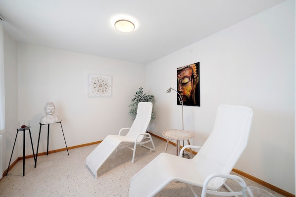 A room with two white lounge chairs, a small table, a Buddha statue, and a framed artwork on the wall.