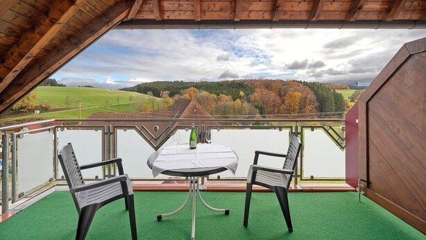 Un balcón con mesa y sillas, vista a un lago y bosque, y techo de madera.