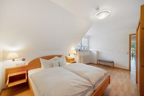 Une chambre avec un plafond en pente, un lit doté d’une tête de lit en bois, des lampes de chevet, un banc et une vue sur l’extérieur.