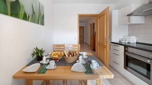 A dining area with a table set for two, a kitchen with modern appliances, and a hallway leading to another room. - Holiday Apartment 'Landblick' with Balcony and Wi-Fi (Biederbach)
