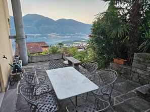 A patio with a table and chairs, a water pump, and a view of mountains and a body of water.