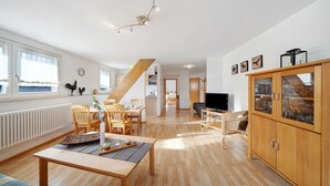 Amplia sala de estar con piso de madera, una mesa de comedor, un sofá, un televisor y un aparador con puertas de vidrio.
