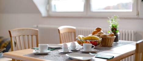 A dining table with breakfast items, chairs, and a window with curtains.