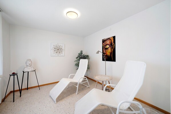 A room with two white lounge chairs, a small table, a Buddha statue, and a framed artwork on the wall.