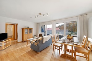 A living room with a sofa, dining table, chairs, a television, and a cabinet. - Holiday Apartment 'Waldblick' with Balcony and Wi-Fi (Biederbach)