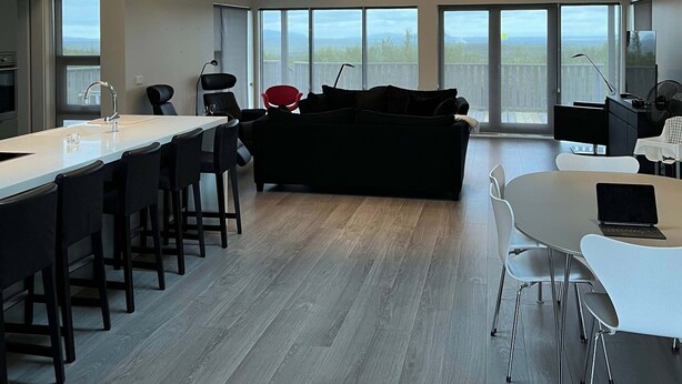 A spacious interior with a high ceiling, skylight, and large windows offering a view of the outdoors. - Golden Circle Cabin – Charming Three Bedroom House (Úthlíð)
