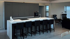A modern kitchen with a central island, bar stools, and a dining area with a table and chairs. - Golden Circle Cabin – Charming Three Bedroom House (Úthlíð)