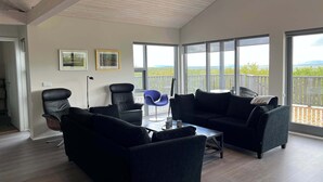 A spacious living area with a high ceiling, large windows, and a balcony with a view. - Golden Circle Cabin – Charming Three Bedroom House (Úthlíð)