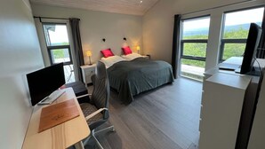 A modern hotel room with a bed, desk, chair, and large windows offering a view. - Golden Circle Cabin – Charming Three Bedroom House (Úthlíð)