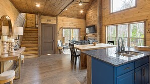 A wooden cabin interior with a kitchen, dining area, and a staircase.