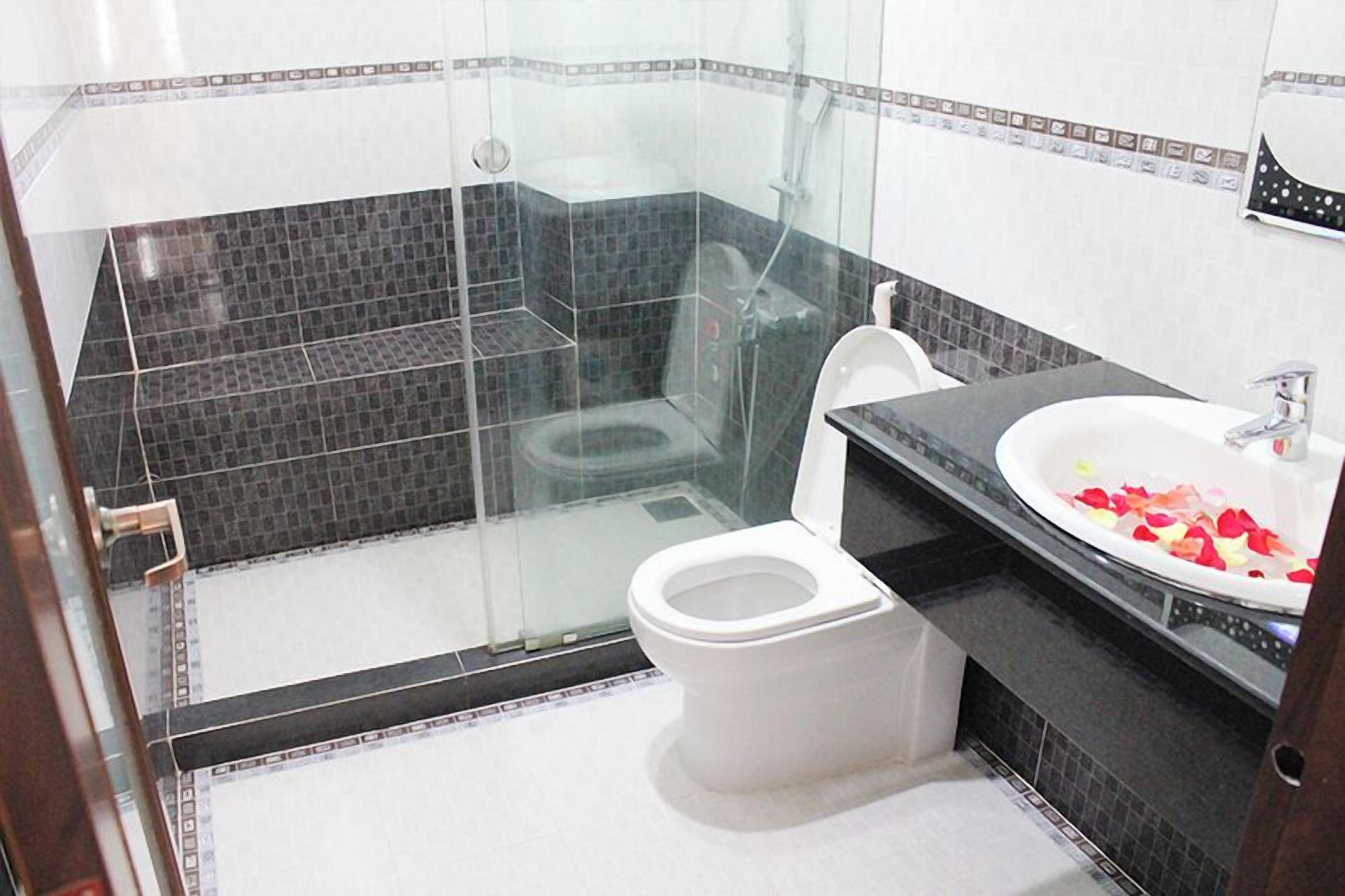 Un baño moderno con ducha de vidrio, inodoro blanco y lavamanos decorado con pétalos de rosa.
