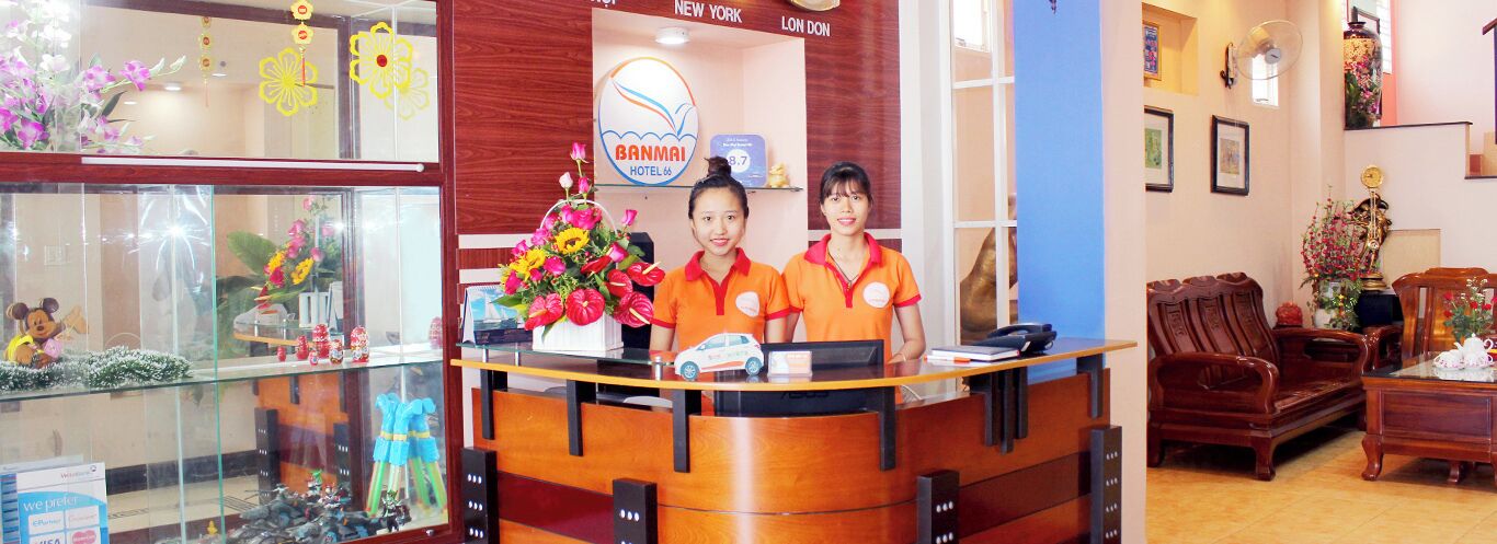 A reception desk with two staff members, a sign for the Banmai Hotel, and a display of toys and flowers.