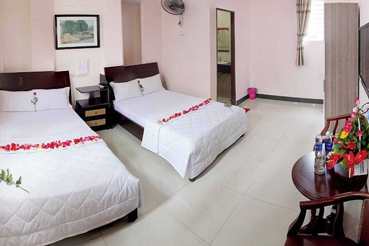 A hotel room with two beds, a bedside table, a mirror, a TV, and a desk with a chair.