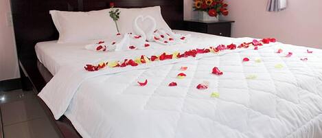 A neatly made bed with a white bedspread and a heart-shaped decoration on the pillow.