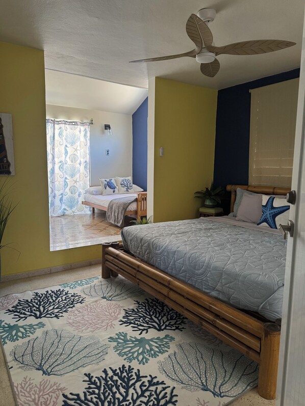 Un dormitorio con cama, ventilador de techo y vista a otra habitación.