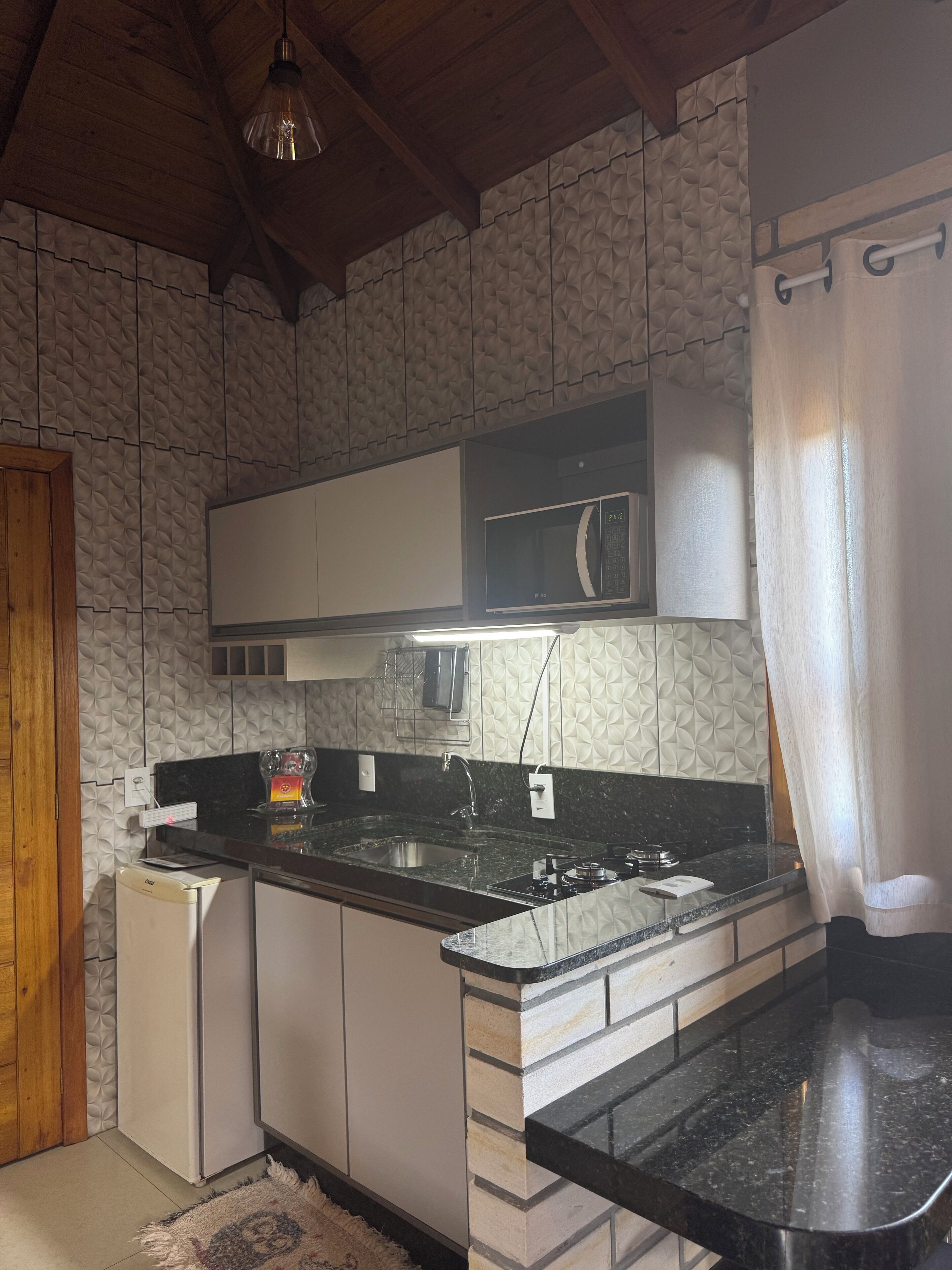 A kitchen with a microwave, sink, and stove. There is a wooden door and a patterned wall.