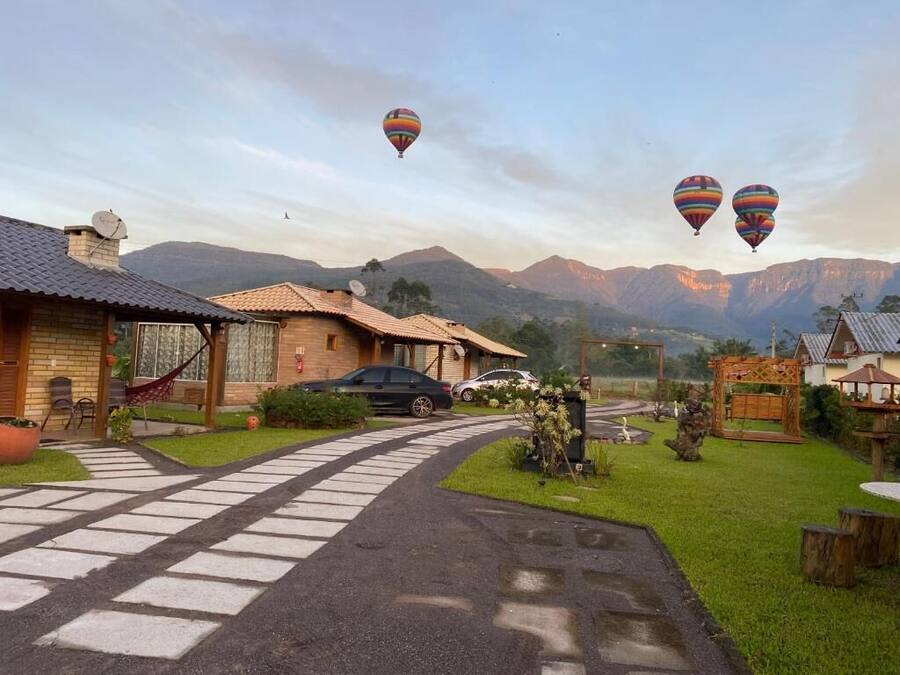 A residential area with a paved driveway leading to a house with a car parked in front. There are hot air balloons in the sky.