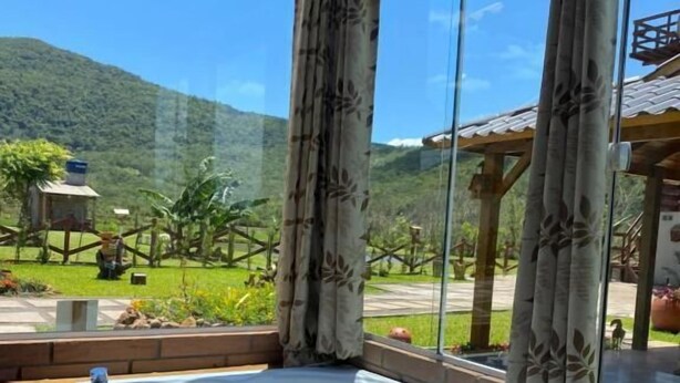 A hot tub with rose petals, champagne, and glasses on a wooden table, with a scenic mountain view through large windows. - Pousada Mirante dos Canyons (Praia Grande)