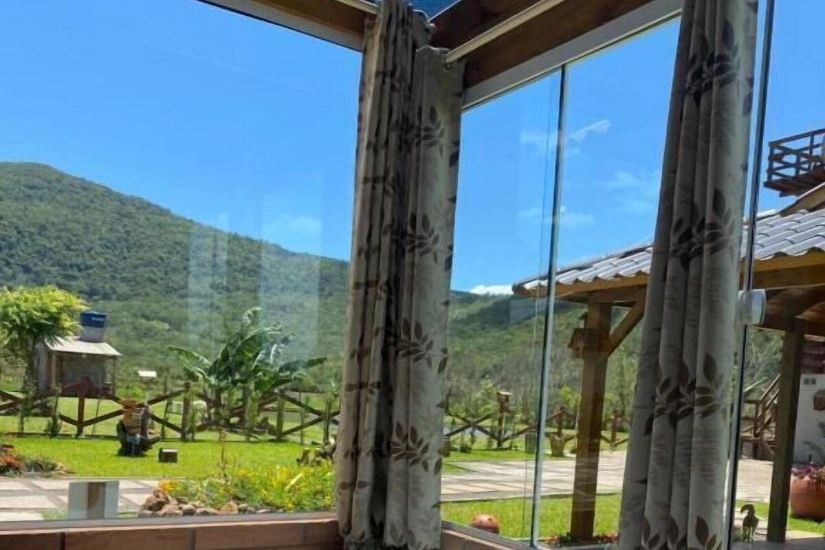 A hot tub with rose petals, champagne, and glasses on a wooden table, with a scenic mountain view through large windows.