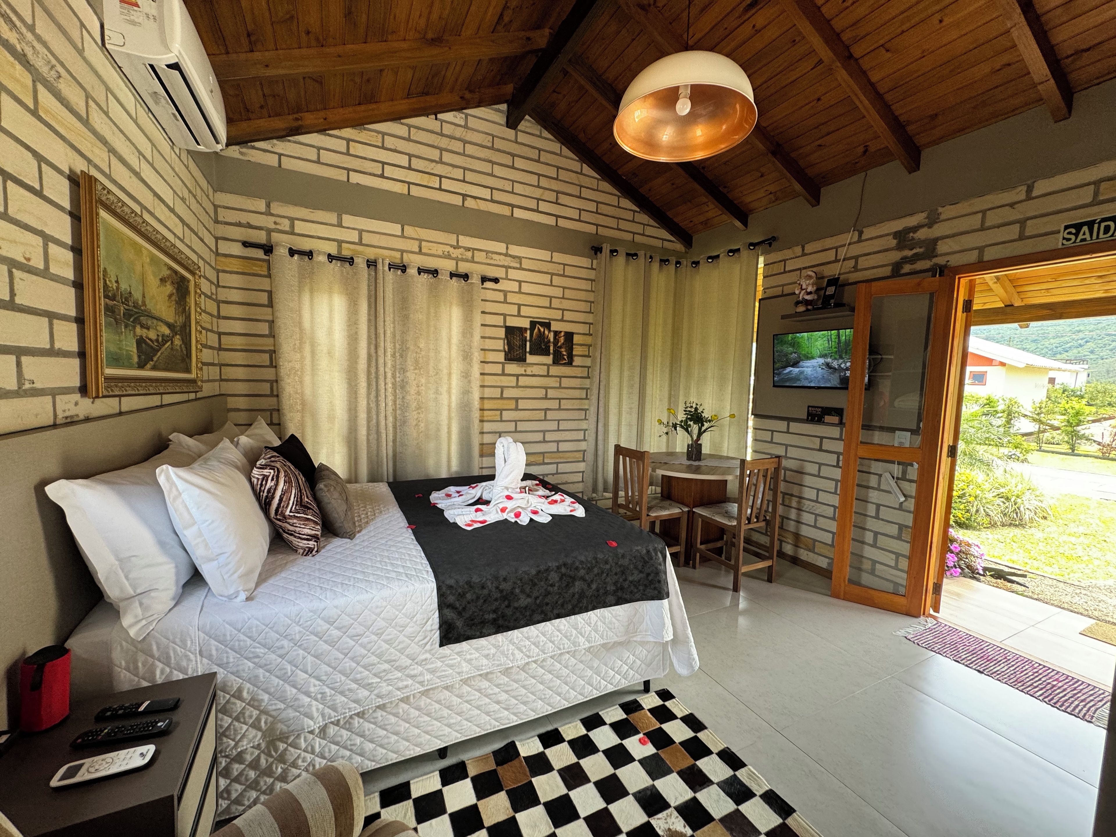 A bedroom with a bed, a desk, a TV, and a view of the outdoors.