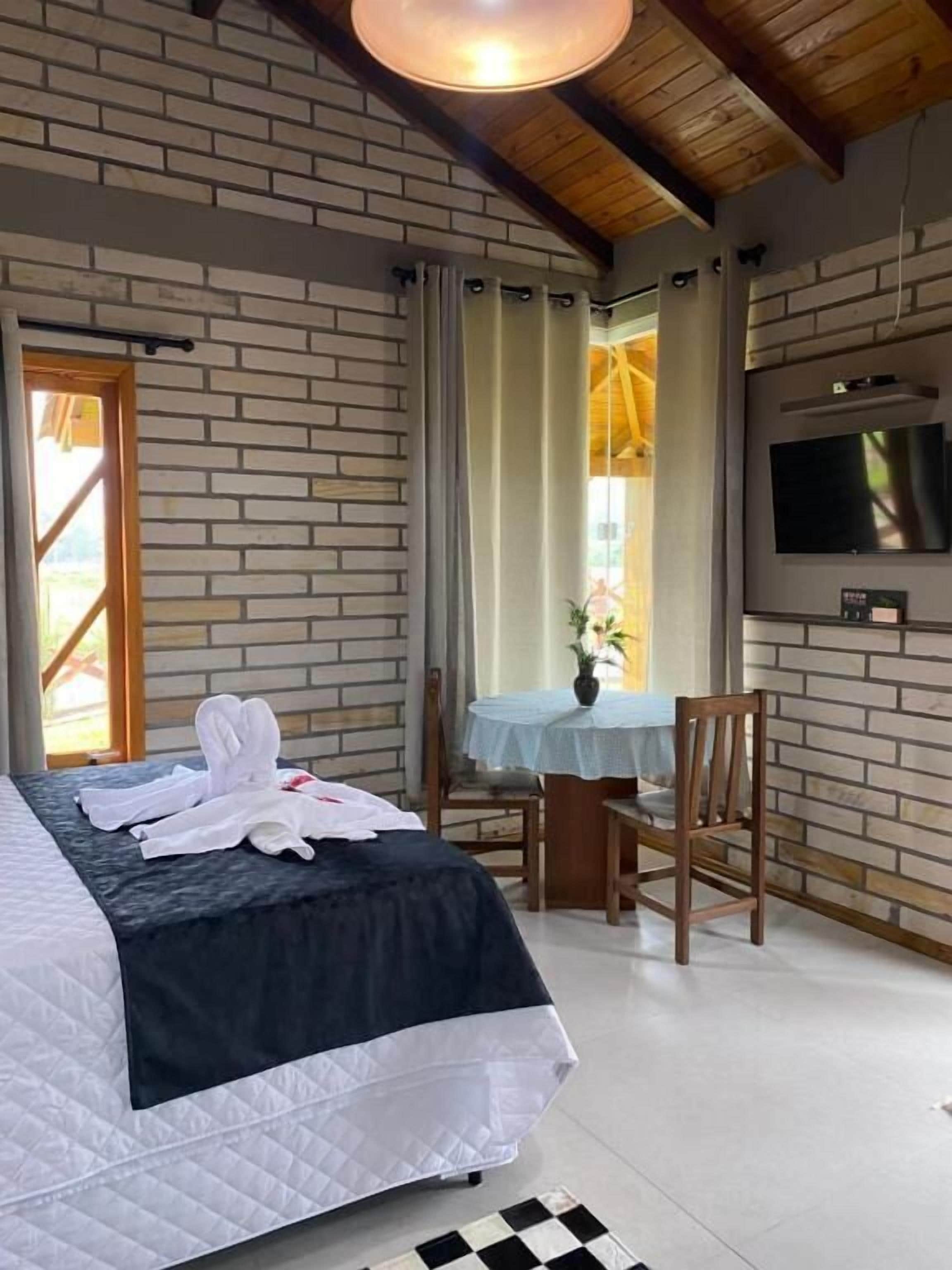 A hotel room with a bed, a desk, a chair, a TV, and a window with curtains.