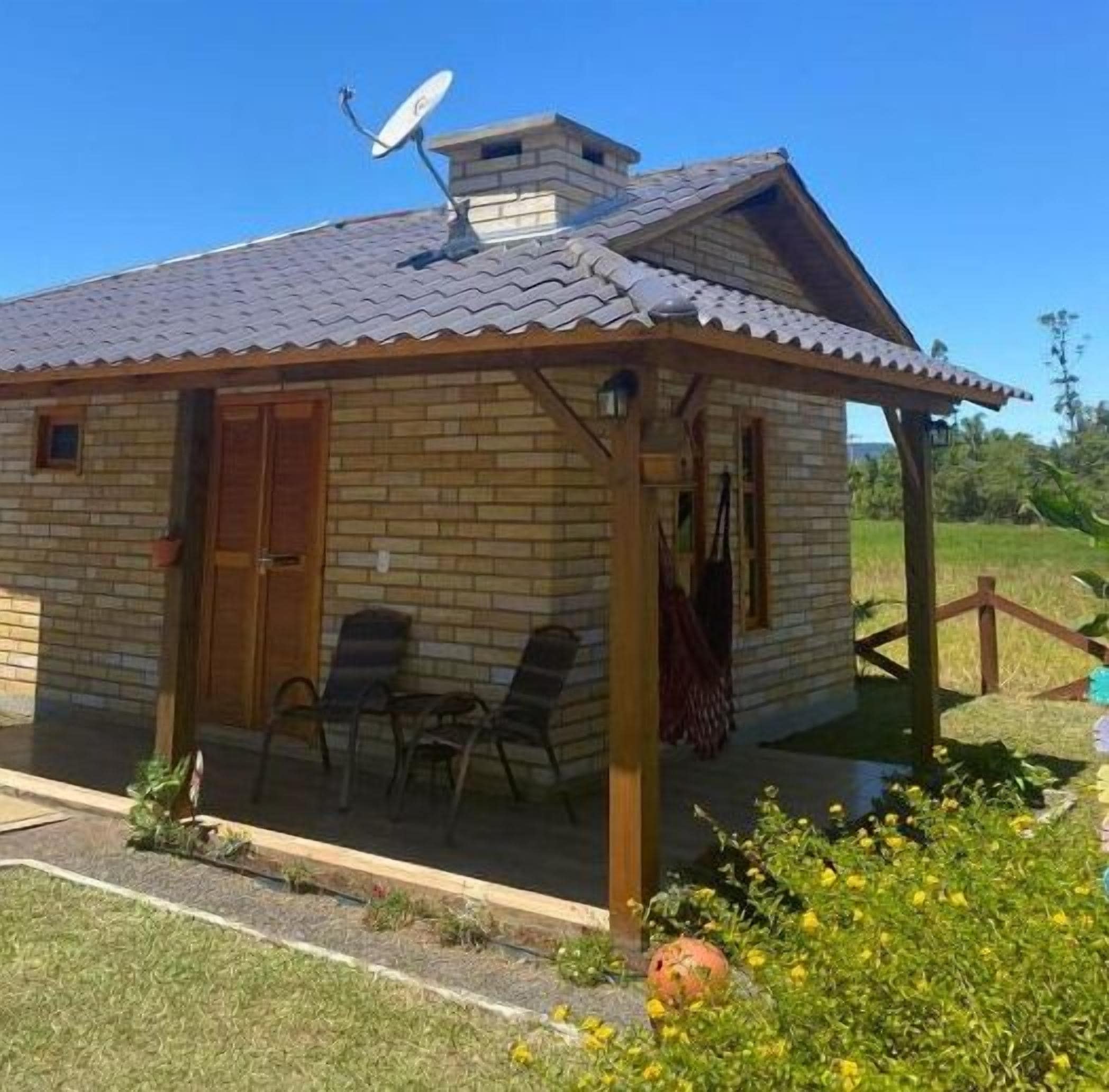 A small brick house with a tiled roof, a satellite dish, and a covered porch with two chairs.