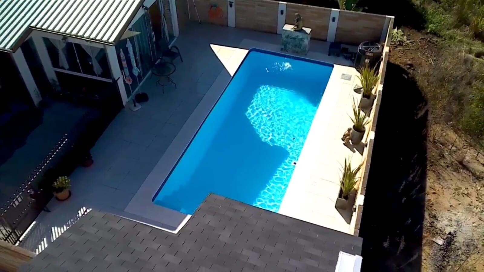 A rectangular swimming pool with a clear blue water surface, surrounded by a paved deck.