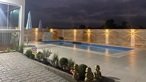 A swimming pool with a brick wall and lights, surrounded by a paved area with plants and a small statue. - Pousada Mirante dos Canyons (Praia Grande)