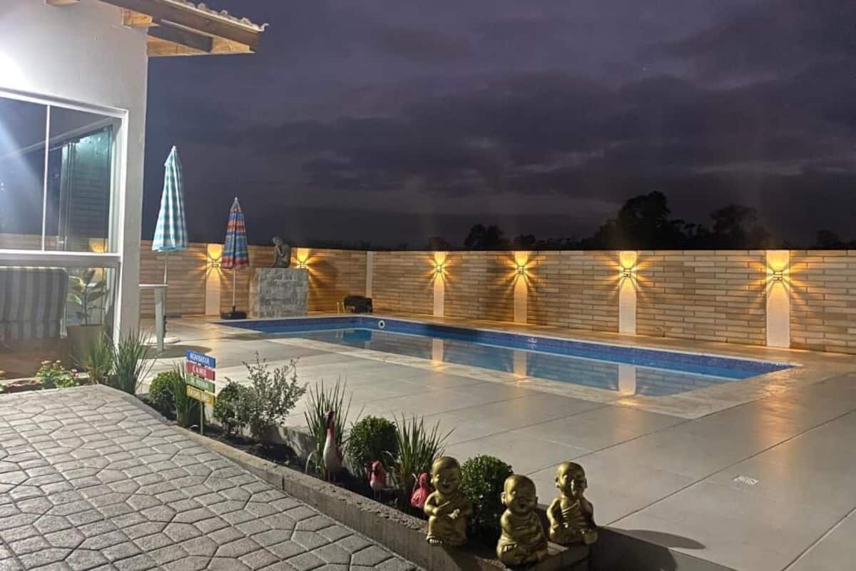 Ein Schwimmbecken mit Backsteinmauer und Beleuchtung, umgeben von einer gepflasterten Fläche mit Pflanzen und einer kleinen Statue.