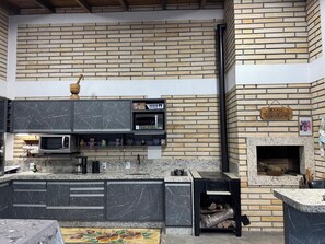 A kitchen with a brick wall, a microwave, cabinets, and a sign that reads 'Canto do Churrasco'. - Pousada Mirante dos Canyons (Praia Grande)