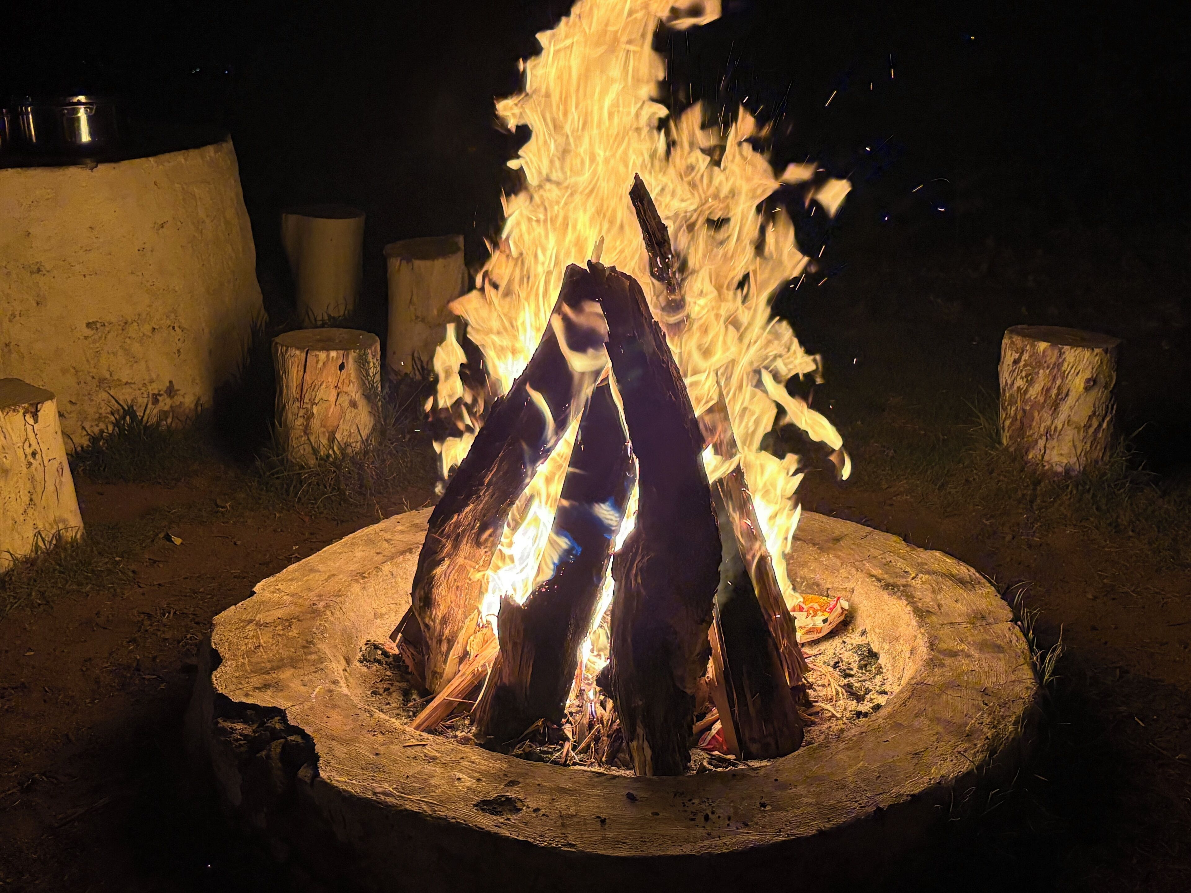 Ein Lagerfeuer mit in Kreisform angeordnetem Holz, umgeben von Holzbalken und einer Betonkonstruktion.