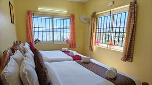 A hotel room with two beds, a window with a view of the hills, a standing fan, and a ceiling fan. - Kodai Hillscape (Kodaikanal)