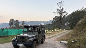 A black off-road vehicle parked on a paved path with a green fence and trees in the background. - Kodai Hillscape (Kodaikanal)