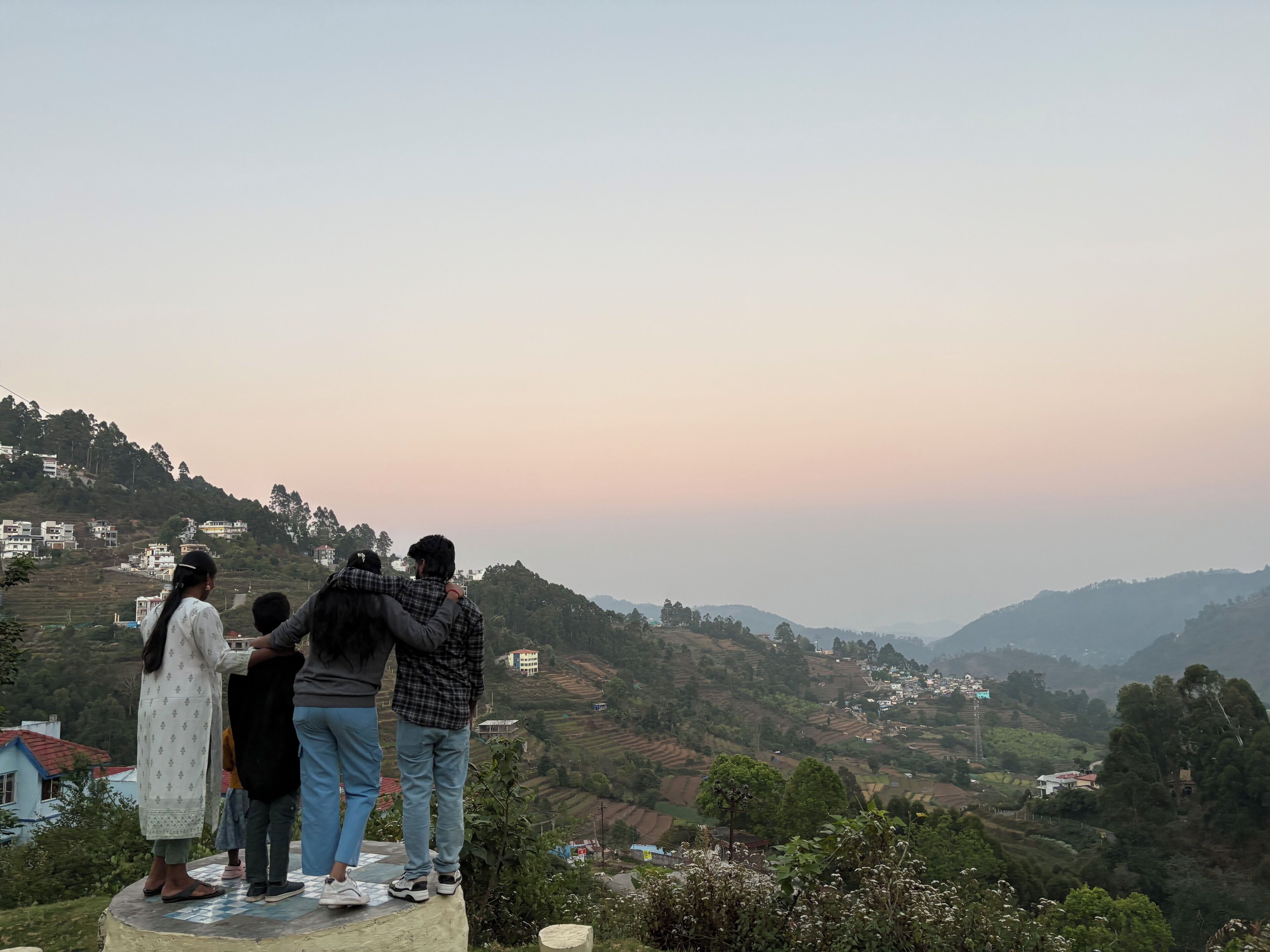A group of people standing on a platform overlooking a hilly landscape with buildings in the distance.