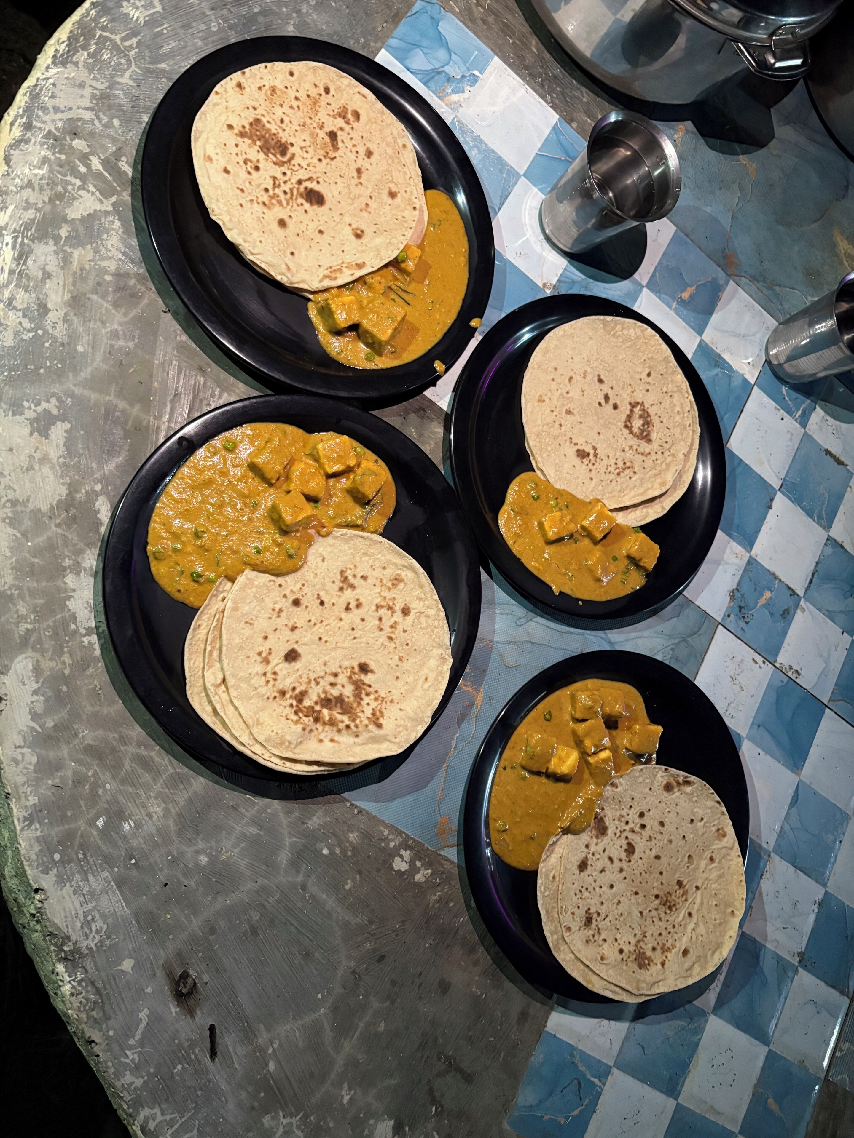 A table with four black plates, each containing a folded flatbread and a portion of curry.