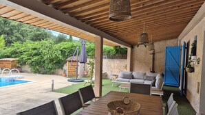 An outdoor patio with a wooden table, chairs, a hanging light fixture, a blue gate, and a pool. - MAISON L'ANGELINE AVEC PISCINE PRIVÉE (Le Plan-de-la-Tour)