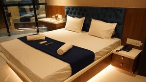 Cama bem arrumada com lençóis brancos e um toque de azul escuro, mesa de cabeceira com abajur e telefone.