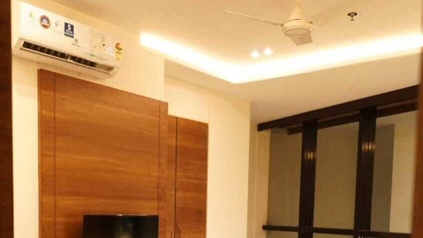 Quarto moderno com cama, TV fixada num móvel de madeira, ar condicionado e janela com persianas.