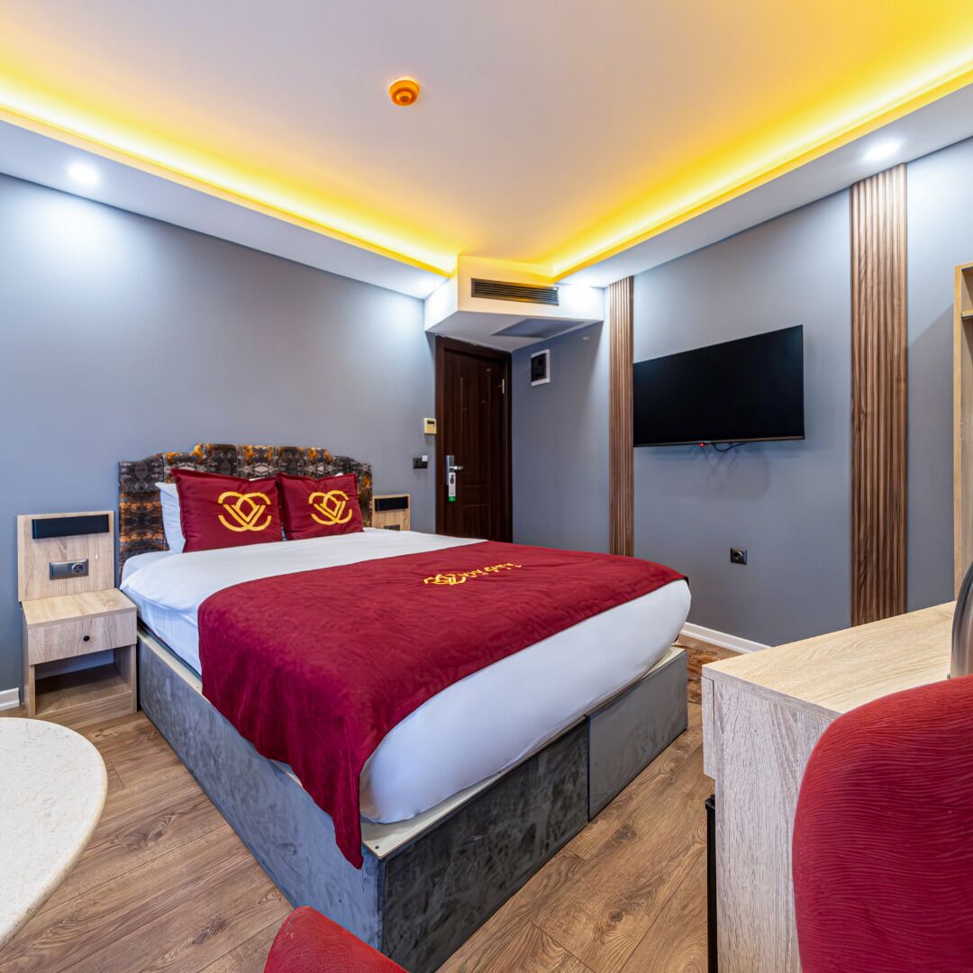 Una habitación de hotel moderna con una cama grande, un escritorio, un televisor de pantalla plana y una lámpara de techo.