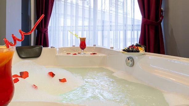 Una bañera con pétalos de rosa, una bebida, un vaso de líquido rojo y un cuenco de fruta.