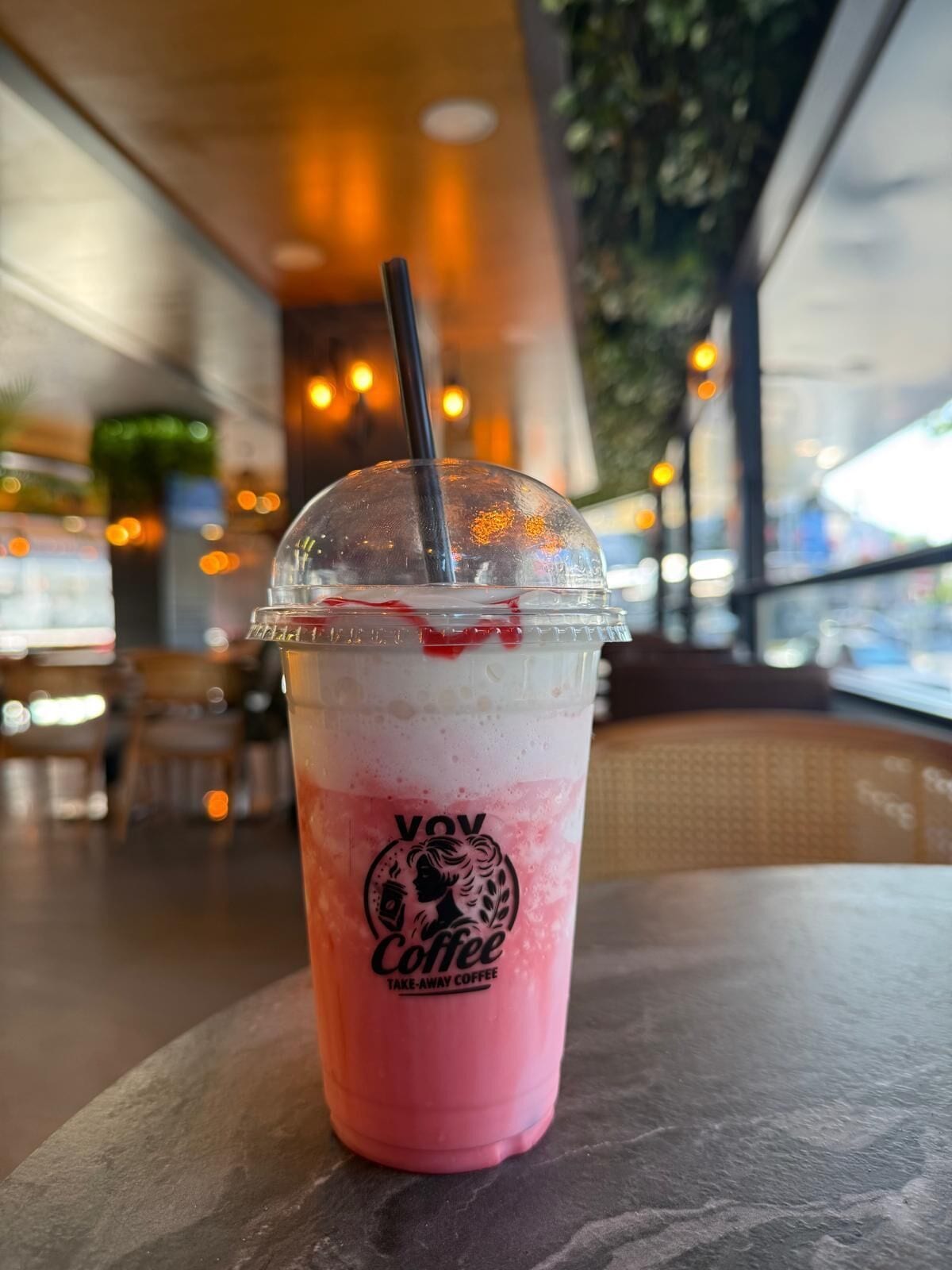 En Vov Coffee kop til afhentning med sugerør på et bord i en café.