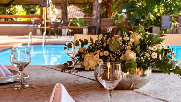 Ein Tisch am Pool mit Blumen, zwei Weingläsern und einer Essgruppe mit Stühlen und Tisch.