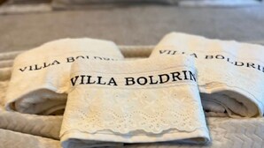 Ein Bett mit einer beigen Bettdecke und zwei gefalteten Handtüchern mit dem Aufdruck "Villa Boldrin".