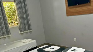 Ein Hotelzimmer mit einem Bett, einem Fenster mit Vorhängen, einer Klimaanlage und einem flachbildfernseher, der an der Wand befestigt ist.