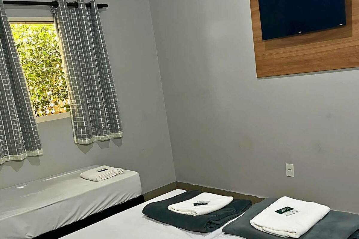 Habitación de hotel con cama, ventana con cortinas, aire acondicionado y un televisor de pantalla plana montado en la pared.