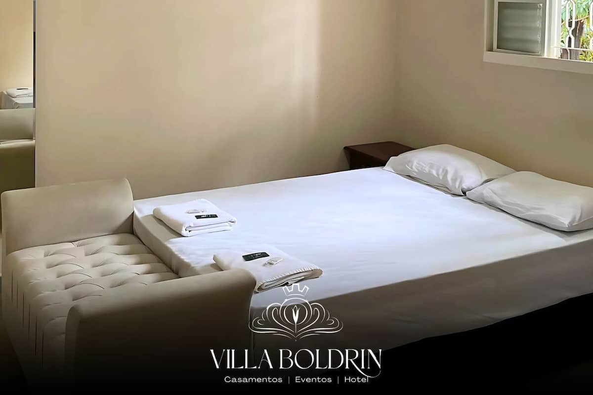 Una habitación de hotel con una cama, una silla, un equipo de aire acondicionado y un ventanal con celosía decorativa.