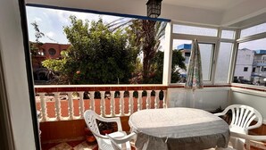 Ein Balkon mit Tisch und Stühlen, Blick auf Gebäude und Bäume sowie eine hängende Laterne.