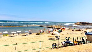 Ein Strand mit Sonnenschirmen, Liegestühlen und einem Steg.